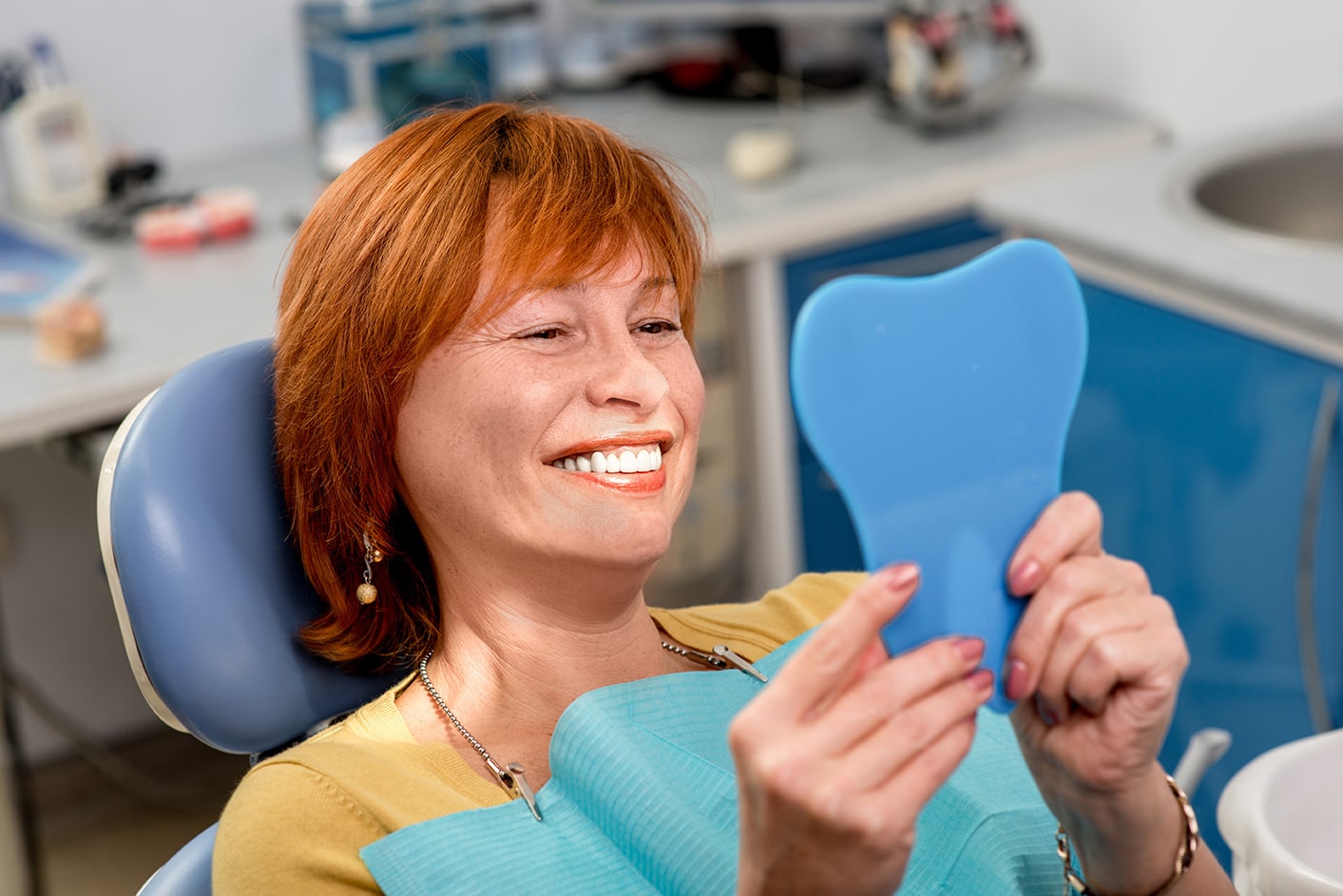 woman smiling in a mirror after denture dentist appointment at smiles only